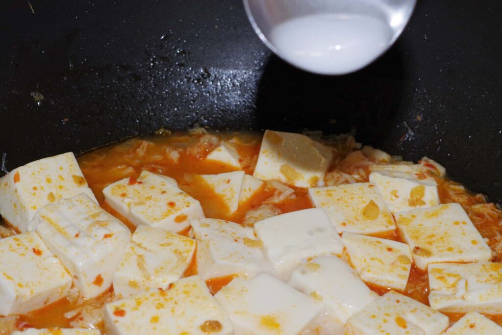 麻婆豆腐の仕上げに鍋へ水溶き片栗粉を加えている様子