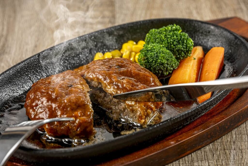 肩バラ肉を使用したハンバーグを鉄板で切るシーン。ジューシーな断面