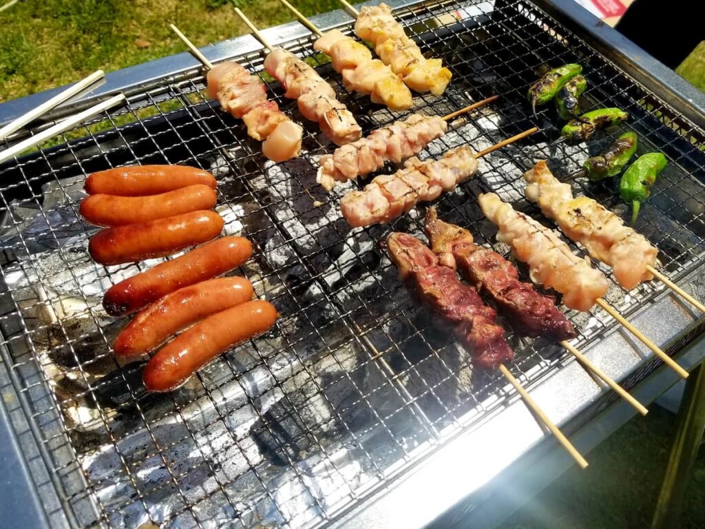 BBQコンロで肉とウインナーを焼いている様子(焼き順と火力調整のイメージ)
