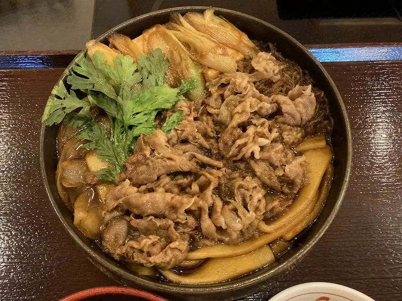 鉄鍋で濃い割り下と生卵を絡めて食べるすき焼きの調理風景