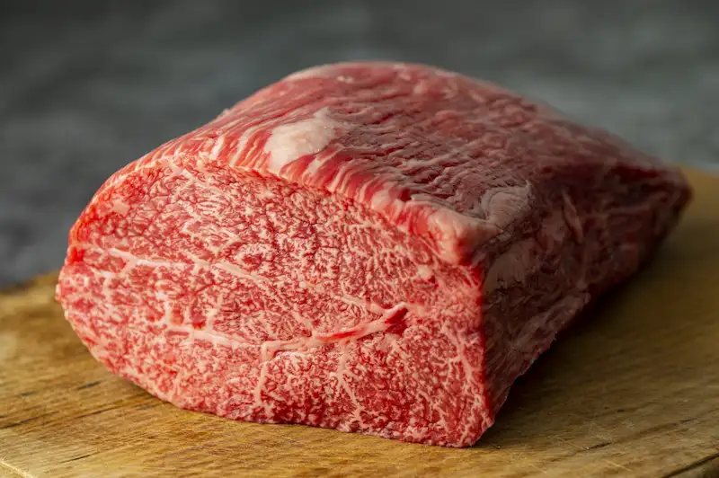 木製のまな板の上に置かれた美しい霜降りサシが入った高級和牛のもも肉