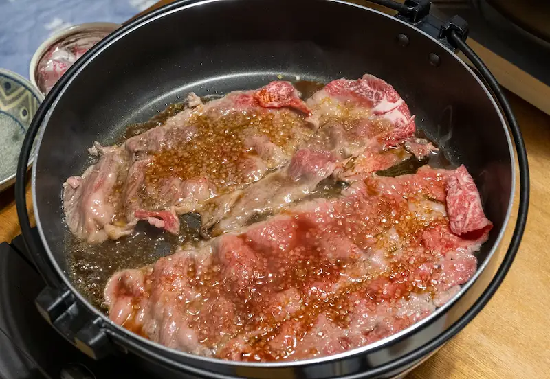 すき焼きの肉をざらめを使って焼いている様子