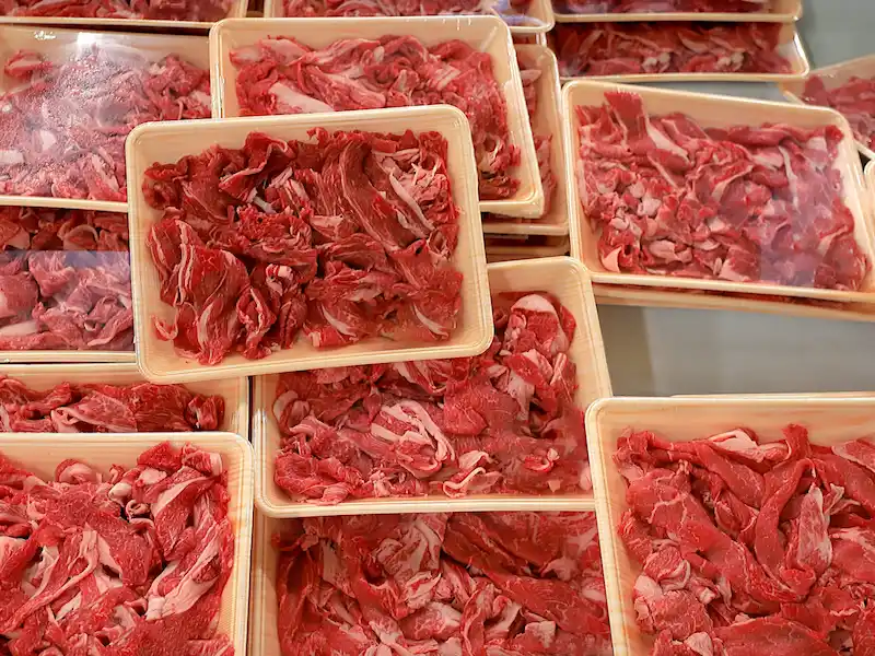 スーパーの精肉コーナーに大量に並ぶプラスチックトレーに入った安価なすき焼き用牛肉のパック