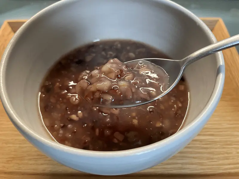 ワンデイクレンズセットのおかゆをスプーンですくったアップ（もち麦・大豆・玄米の粒ととろみ）